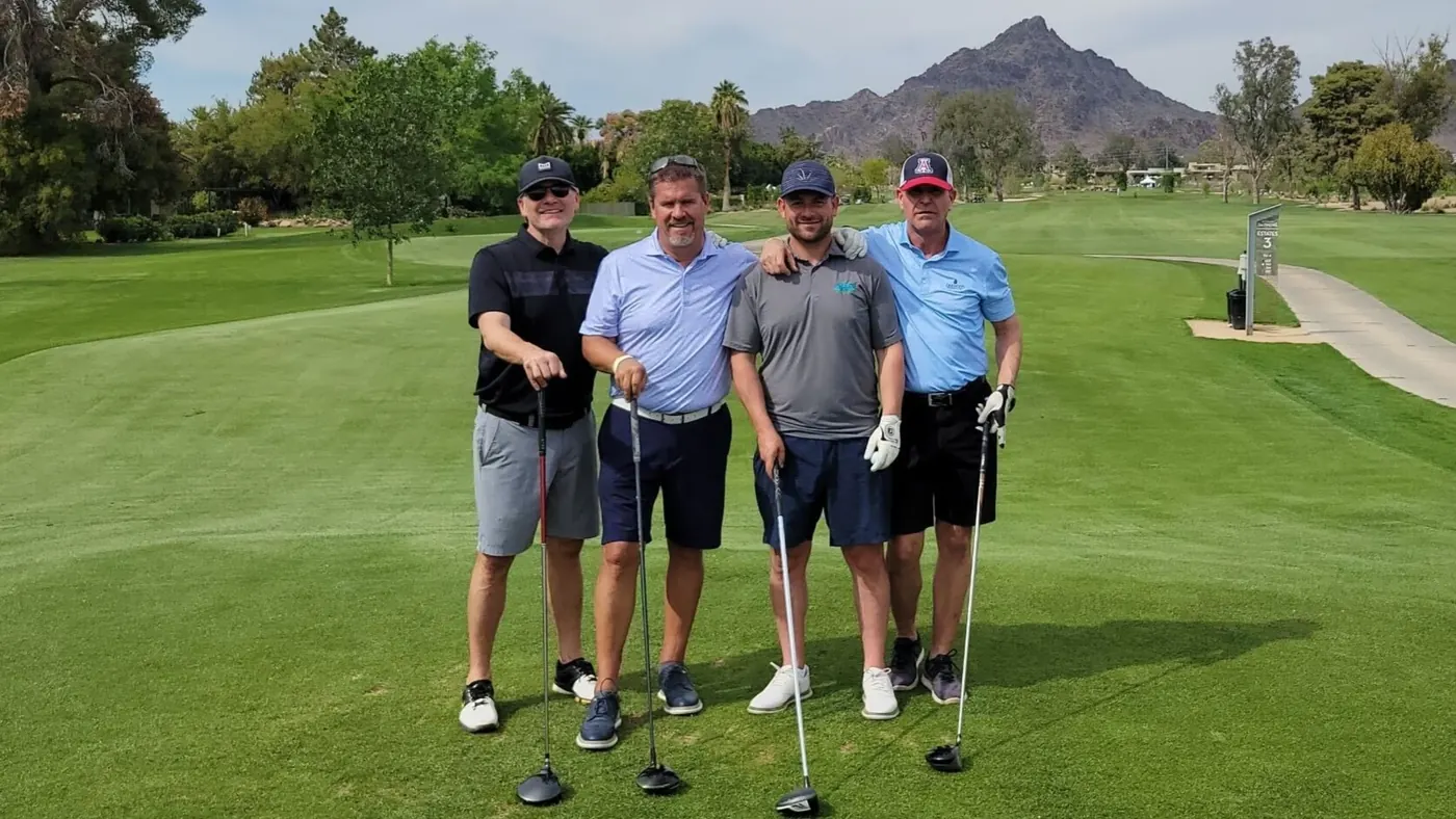 Four golfers with their drivers on the fairway, a desert peak behind them, at the BOMA golf tournament