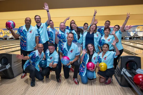 Encore team in matching light blue bowling shirts cheering at the lanes