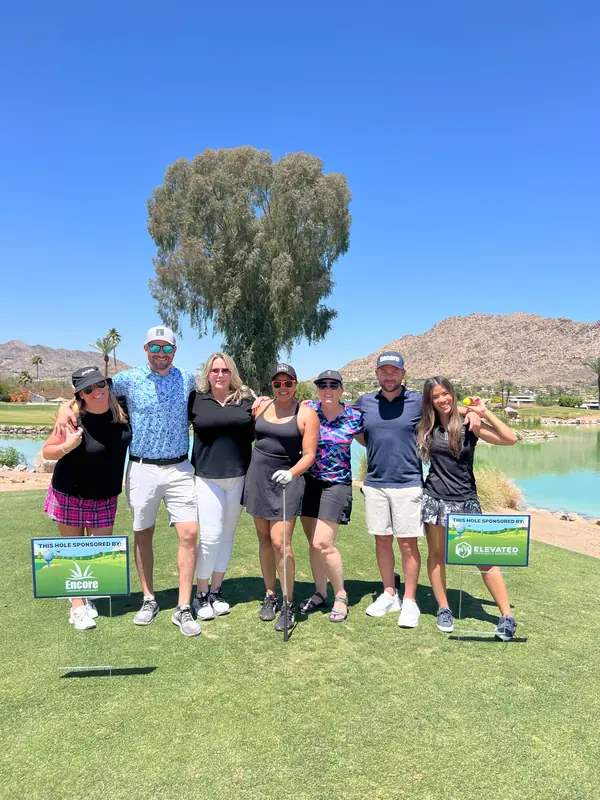 Golfers posing by a tree with tournament sponsor signs at the Encore Invitational