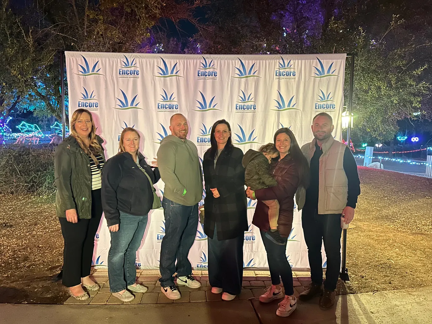 Encore team and clients in front of an Encore step-and-repeat backdrop at ZooLights client appreciation night