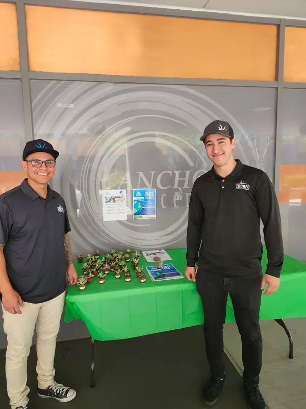 Two Encore team members standing beside a plant giveaway table at an Earth Day event