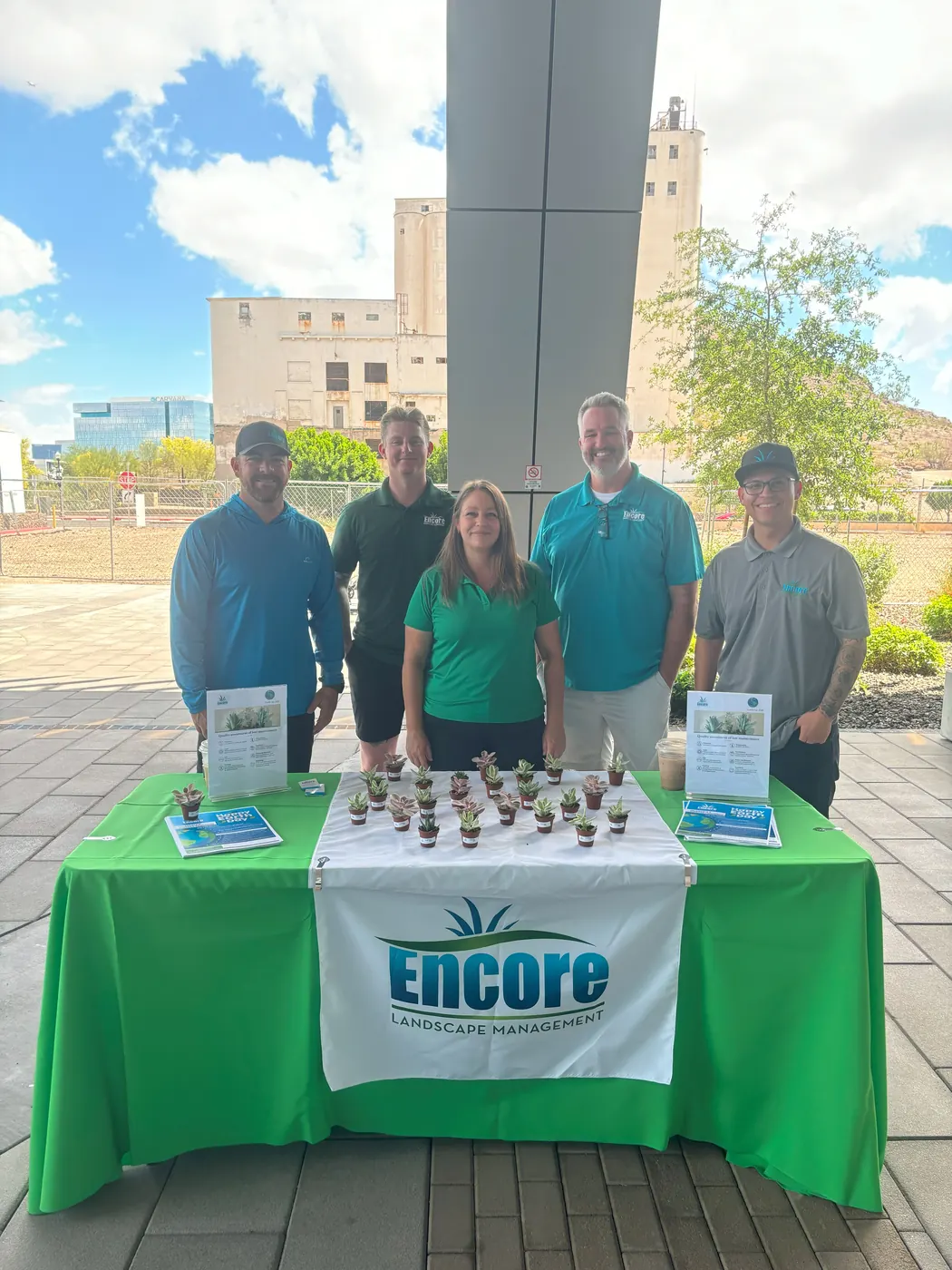 Encore team at an Earth Day booth with a green Encore tablecloth and potted plant giveaways