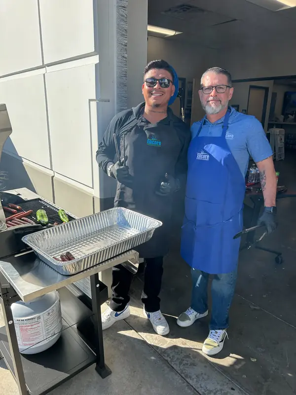Two Encore team members in aprons grilling at an employee cookout
