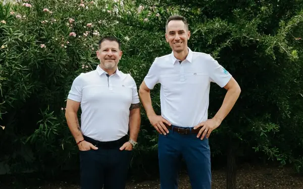 Encore's co-owners standing in front of a green hedge