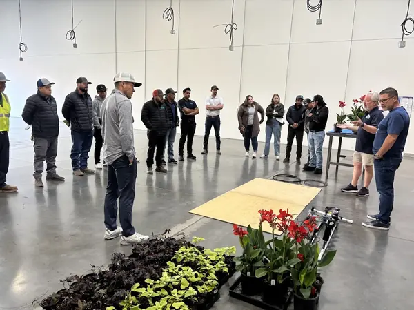 Crew members at an indoor flower-installation training with trays of seasonal plants