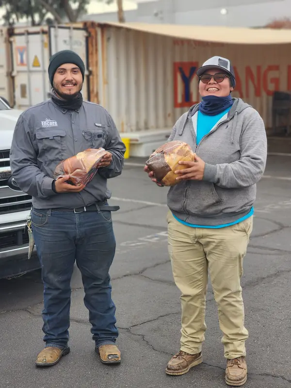 Two Encore crew members each holding a holiday ham in the yard