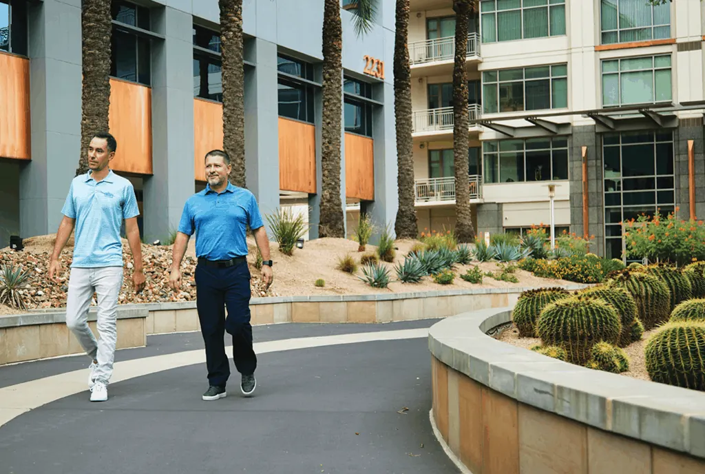 Two Encore leaders in blue polos walking past a barrel cactus bed at a client property
