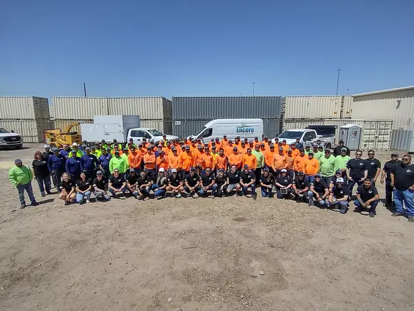 Large group photo of the Encore team, most in orange crew shirts, in the company yard
