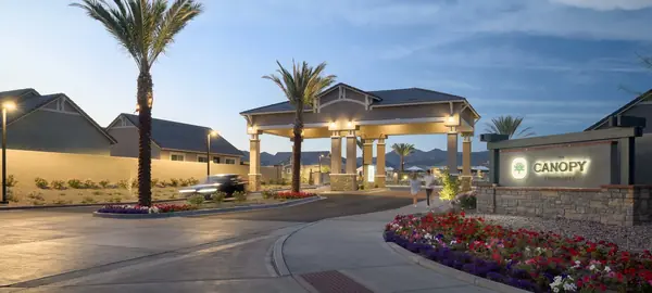 Entrance drive at Canopy at Sundance at dusk, with tall palms, a lit gazebo and red seasonal flower beds by the monument sign