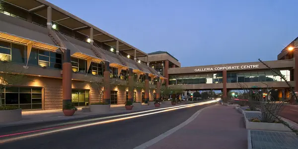 Street view of Galleria Corporate Centre at dusk, with landscaped medians and the sky bridge over the road