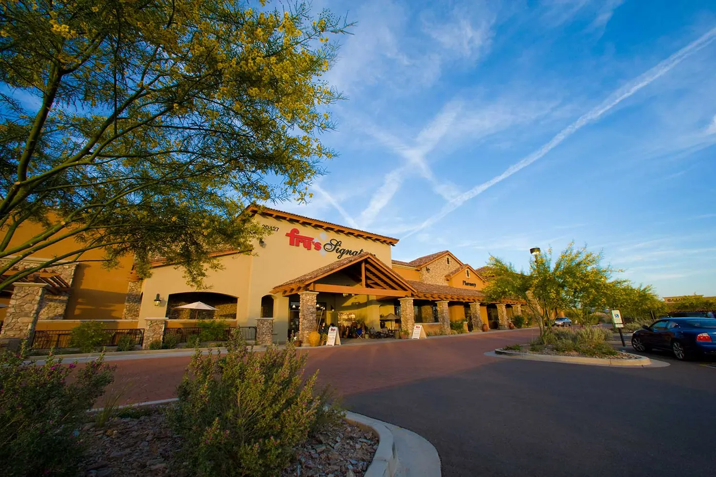 Desert trees and shrubs framing the storefronts and entry drive at Hayden Peak Crossing