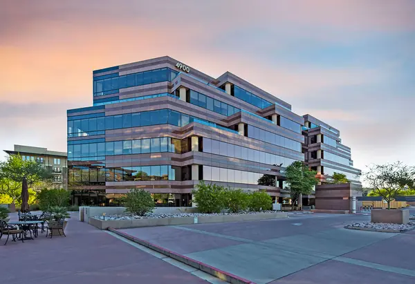 Glass office building at Portales Corporate Center with a palm-lined plaza and planters at sunset