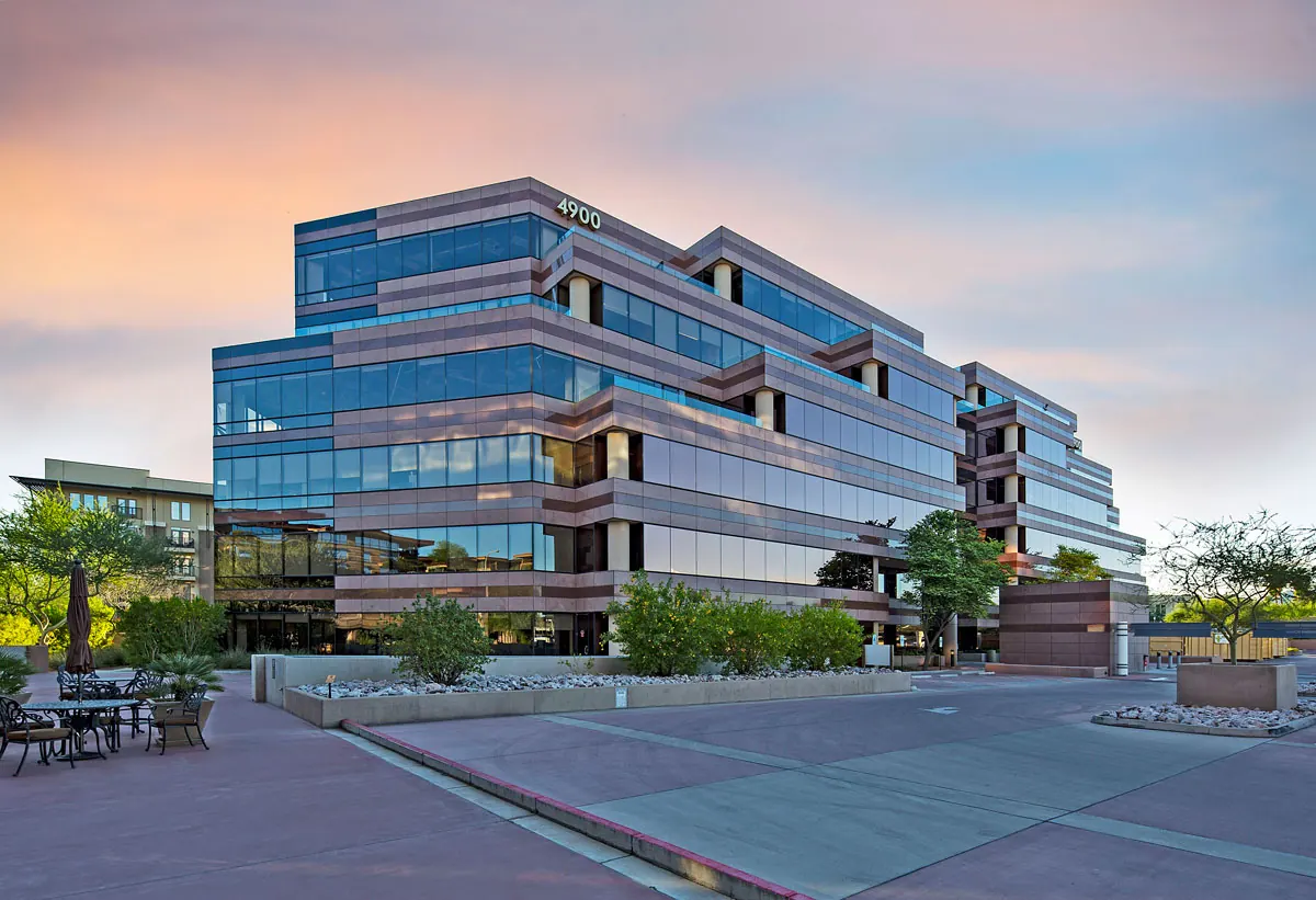 Glass office building at Portales Corporate Center with a palm-lined plaza and planters at sunset