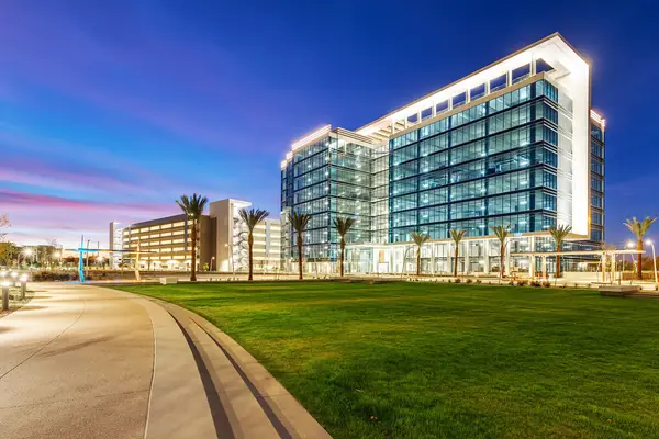 The Grand at Papago office tower at twilight, with a broad green lawn and a row of palms along the walkway